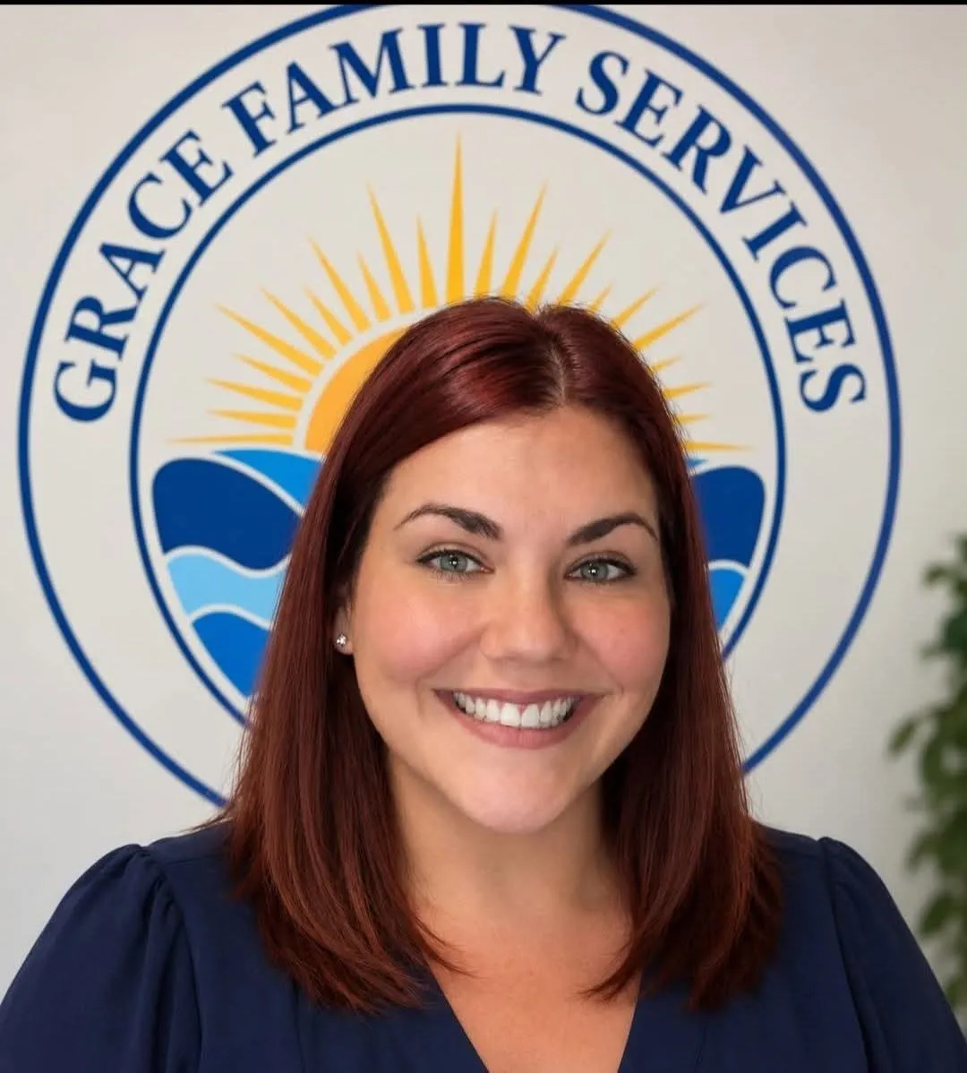 Ashley Riddick, Community Engagement Coordinator, smiling in front of the Grace Family Services logo mural