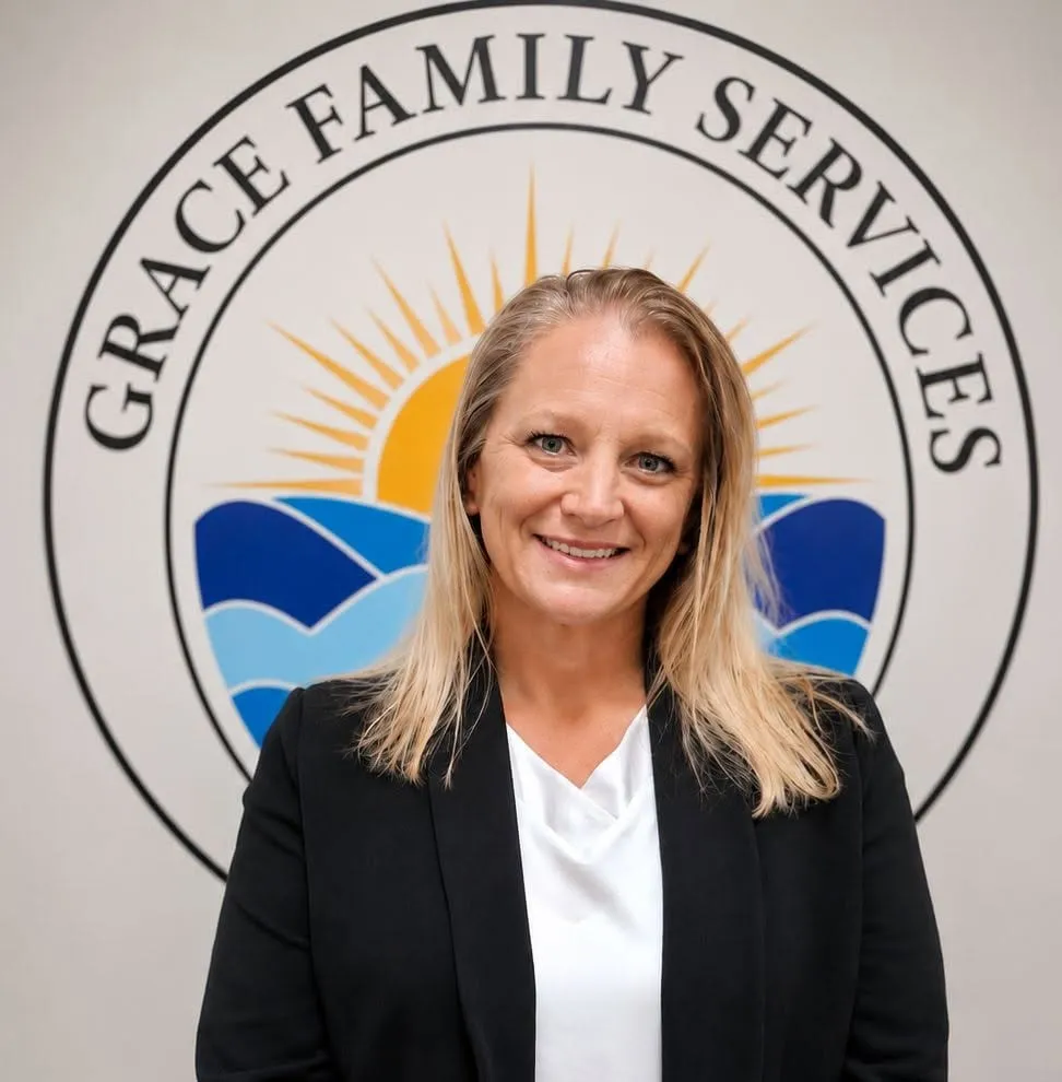Mindy, Clinical Director, smiling in front of the Grace Family Services logo mural