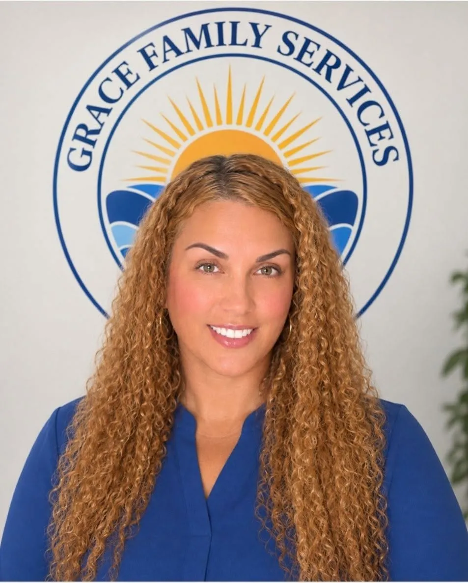 Raberta, therapist, smiling in front of the Grace Family Services logo mural