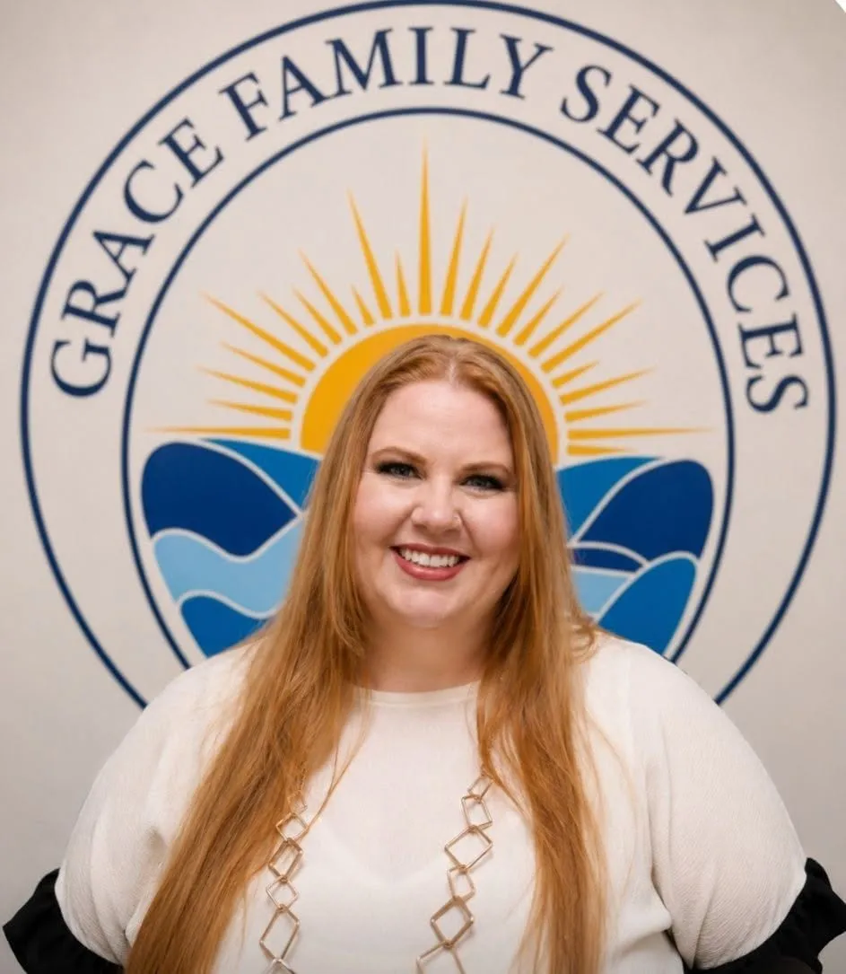 Shanin, Licensed Professional Counselor, smiling in front of the Grace Family Services logo mural